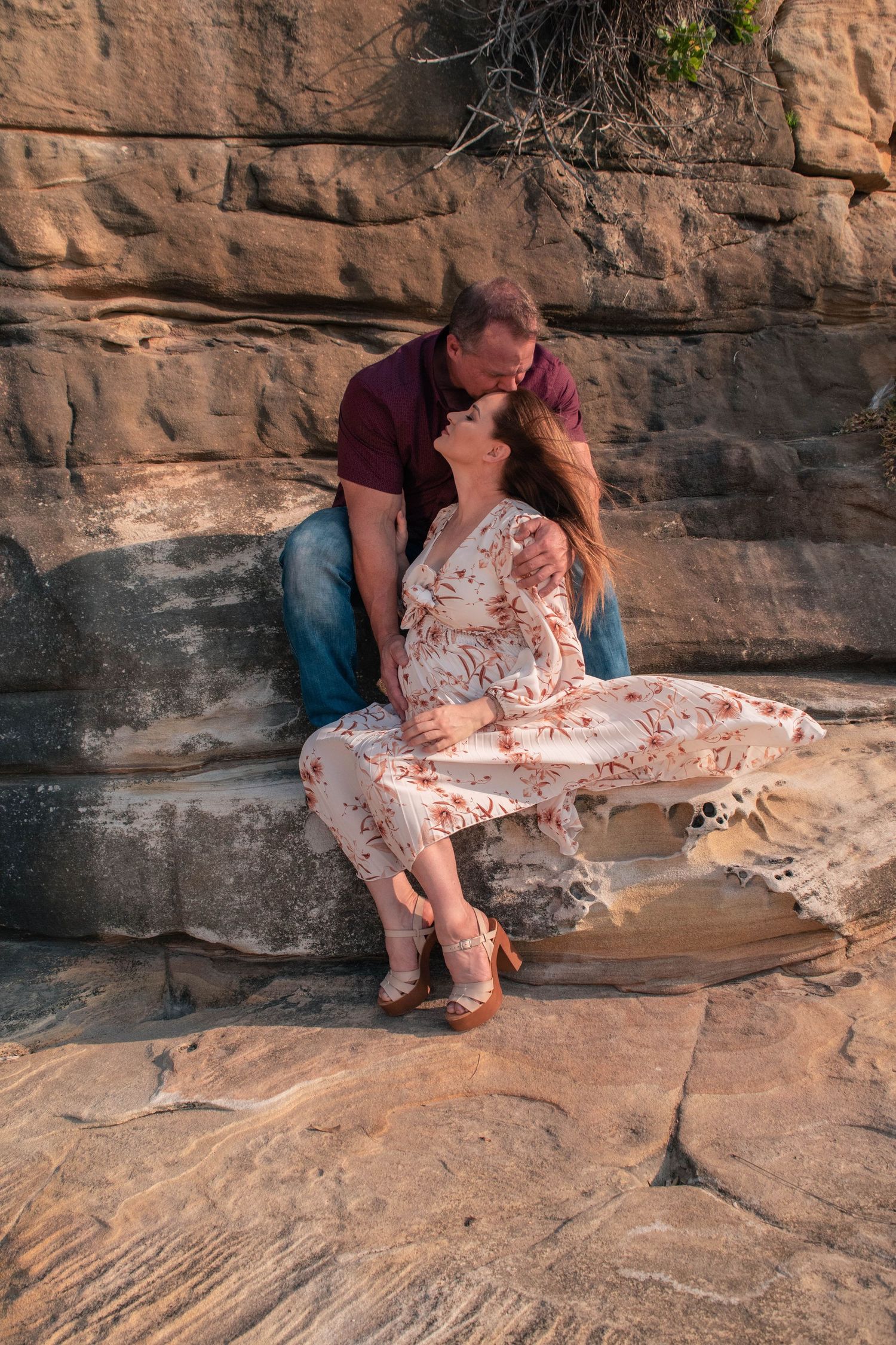 Intimate maternity photography session captured on rugged rocky terrain at sunset.