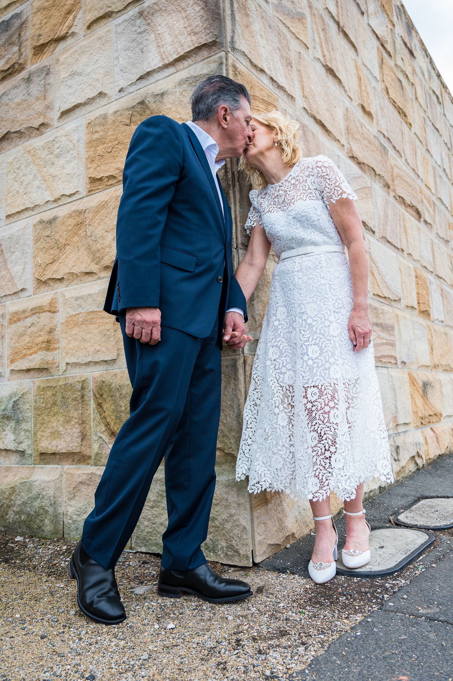 Tender moment against sandstone wall with elegant lace dress and navy suit.