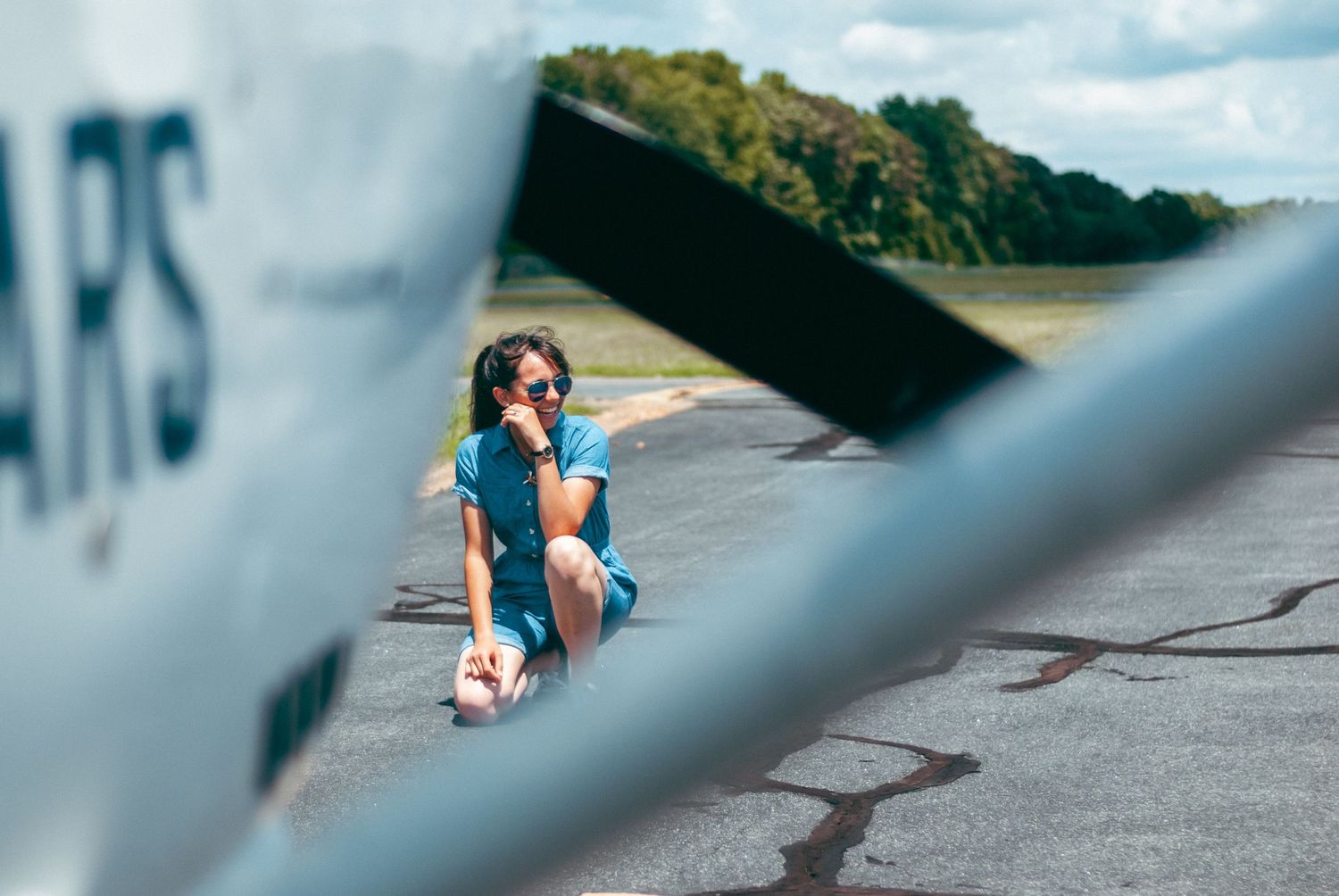 Woman crouching on the ground seen through the wing and propeller of an airplane