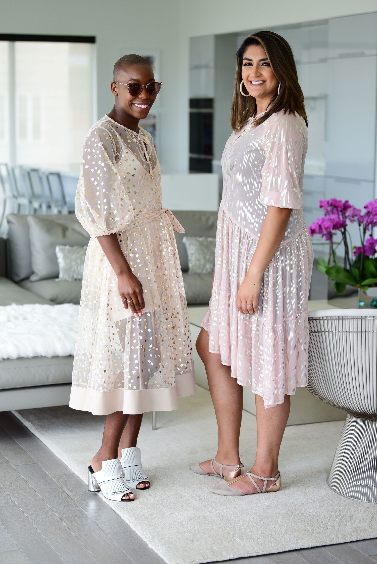Friends in matching light summer dresses posing in elegant white interior.