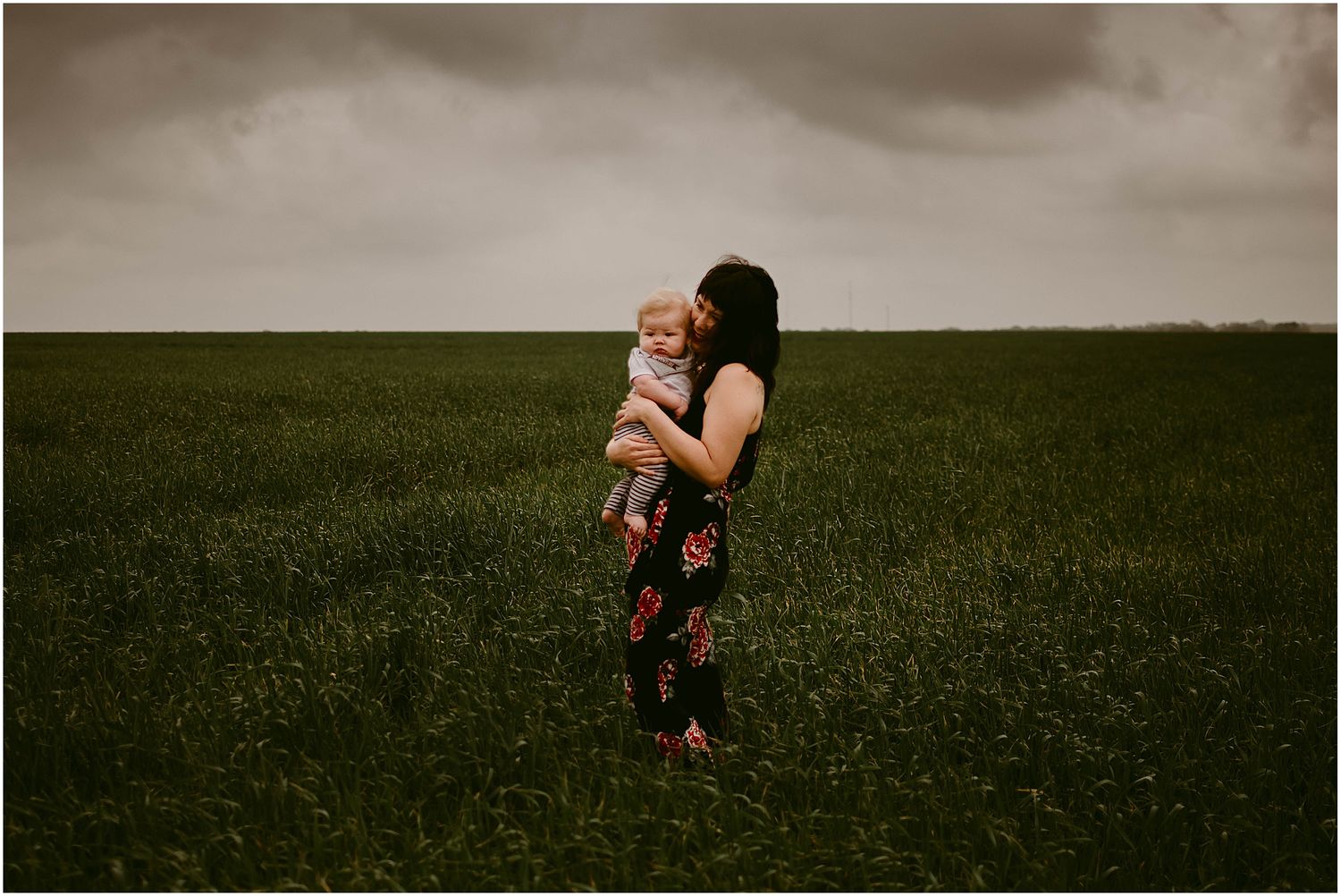 Two silhouettes share a tender moment against dramatic storm clouds in an open field.