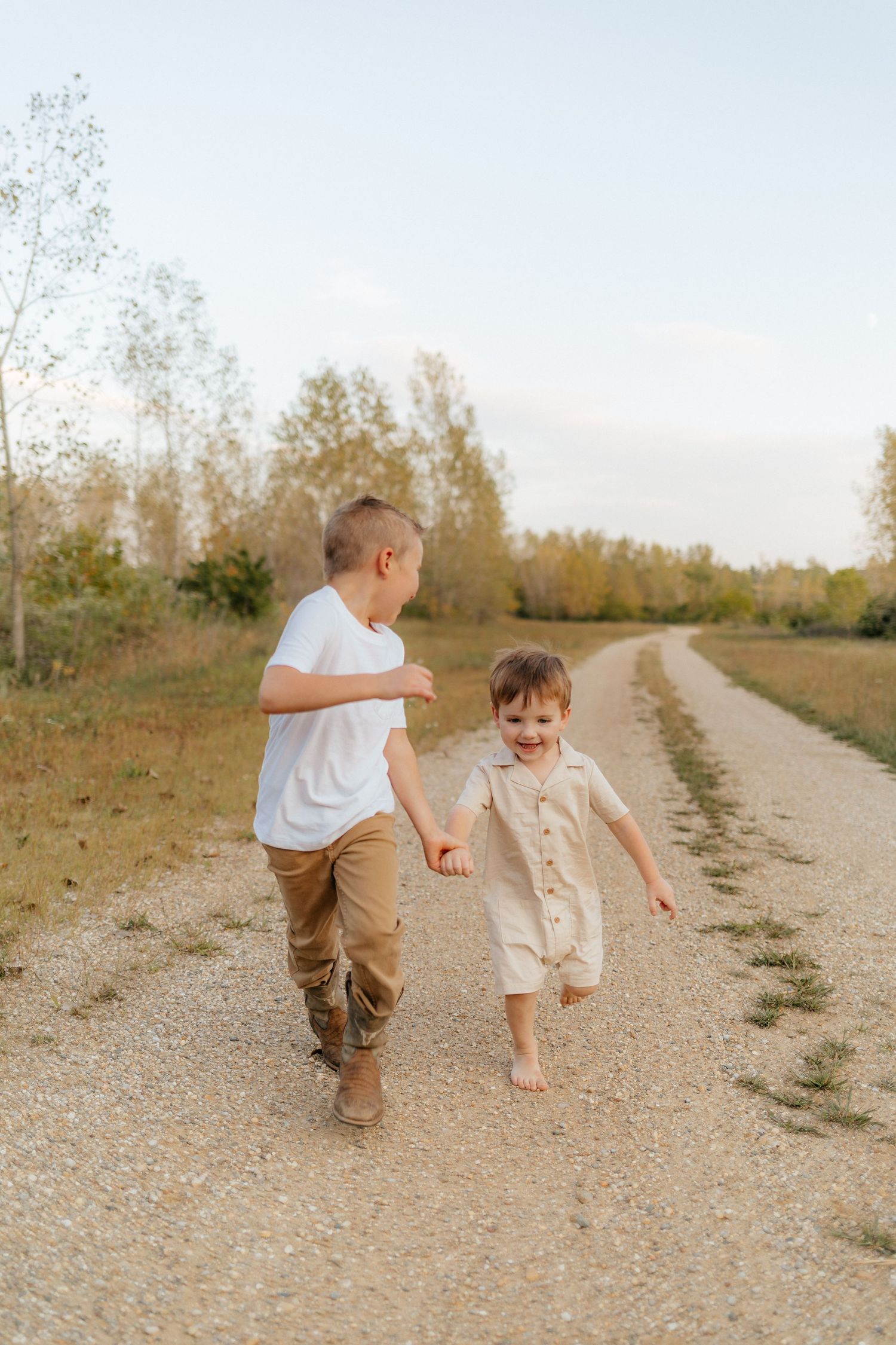 Two children running and laughing together on a dirt path surrounded by autumn trees.