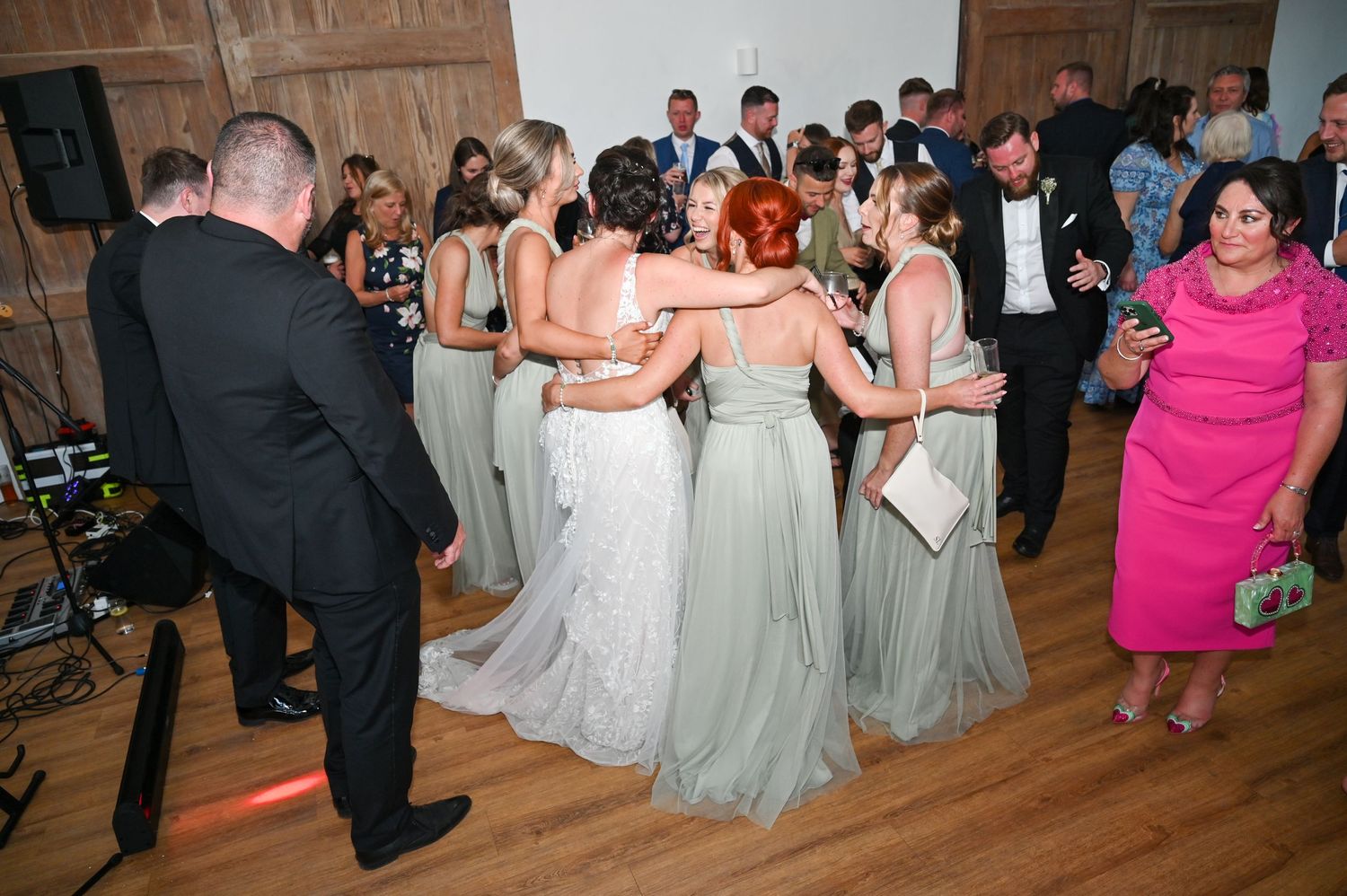 Wedding party dancing together in teal bridesmaid dresses on a hardwood floor.