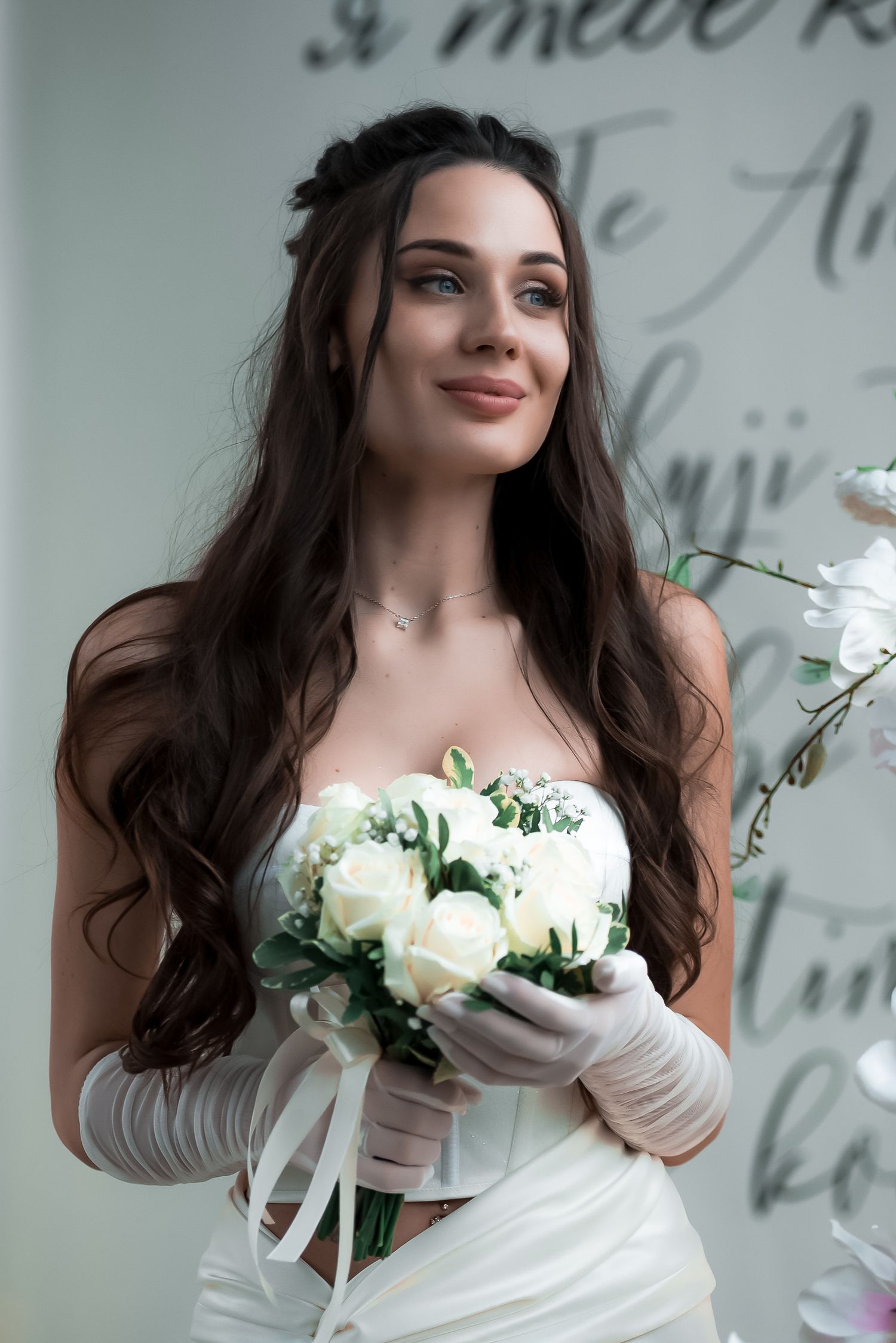 Bridal portrait with white roses and long dark hair against a light background.