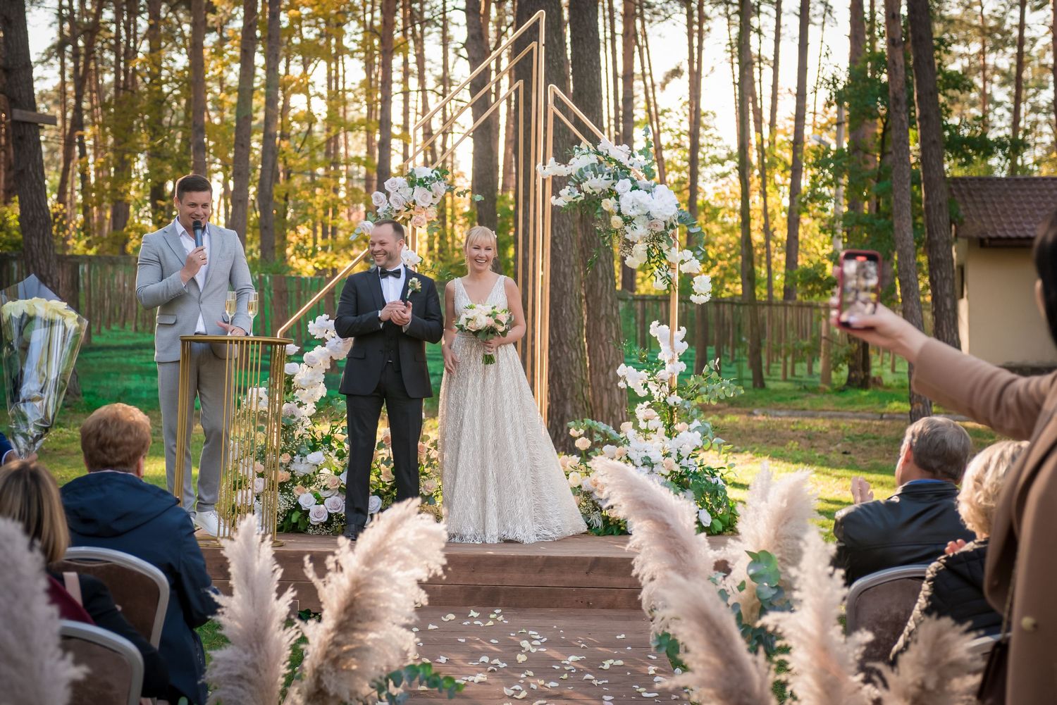 Outdoor wedding ceremony in a forest setting with guests and natural lighting.