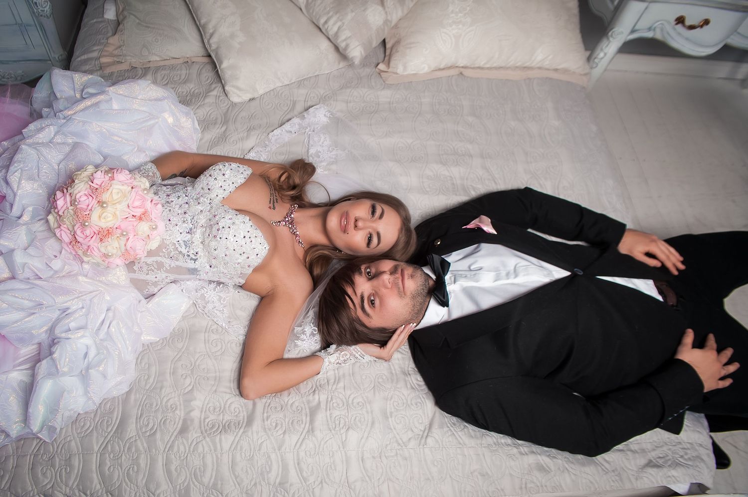 Wedding couple lying down in formal attire on white fabric.