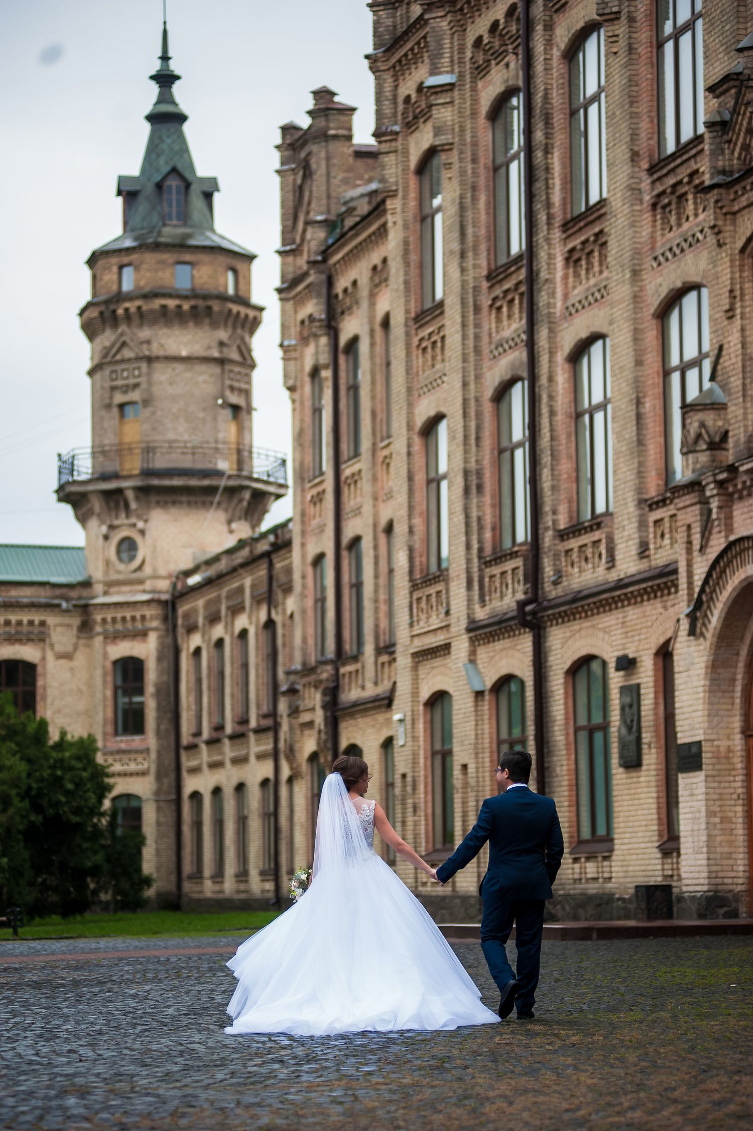 Wedding couple poses in front of historic gothic architecture with ornate stone facades and towers.