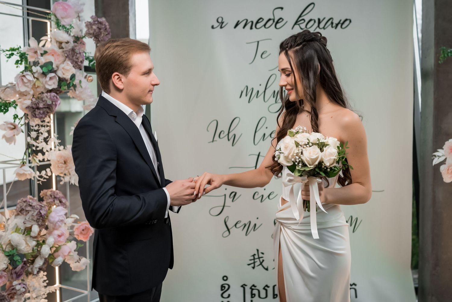 Intimate wedding ceremony moment in front of a wall with multilingual love messages.