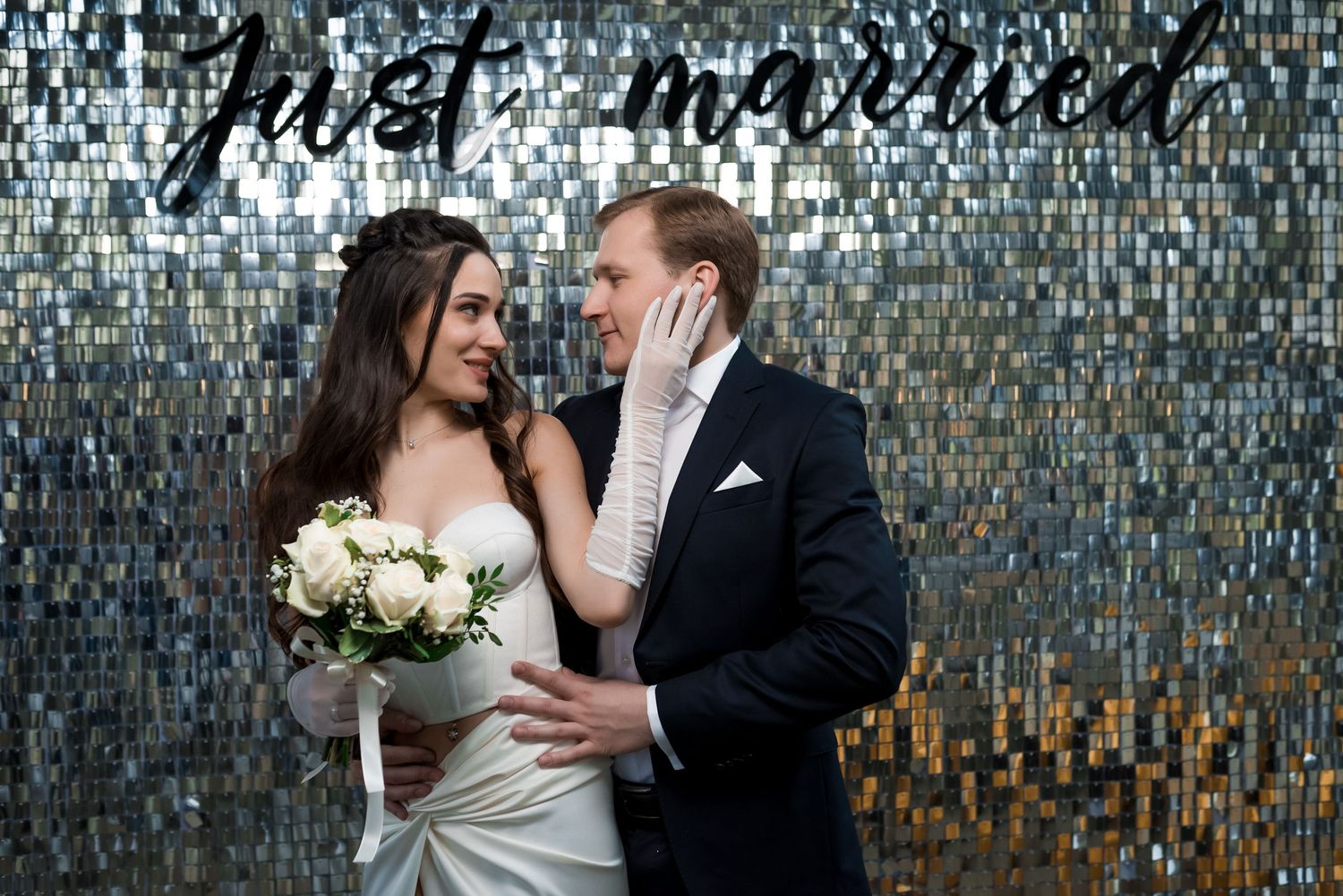Romantic wedding couple poses against a sparkling mosaic wall background.