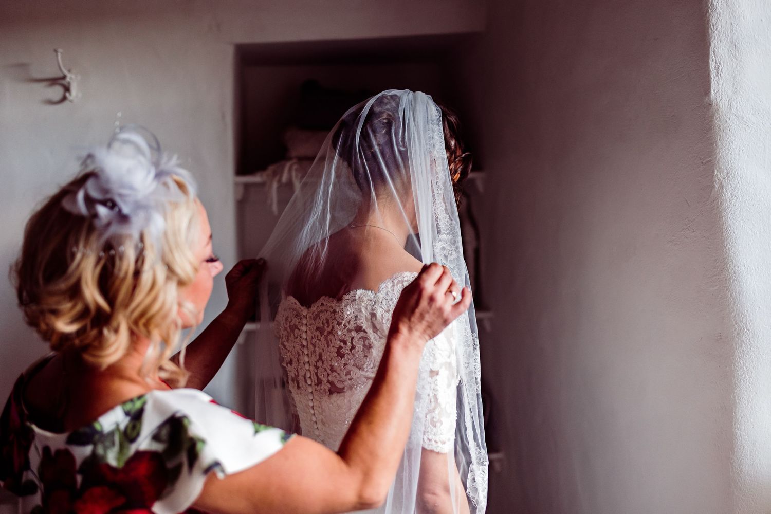 Delicate adjustments being made to a white lace wedding veil in soft natural lighting.