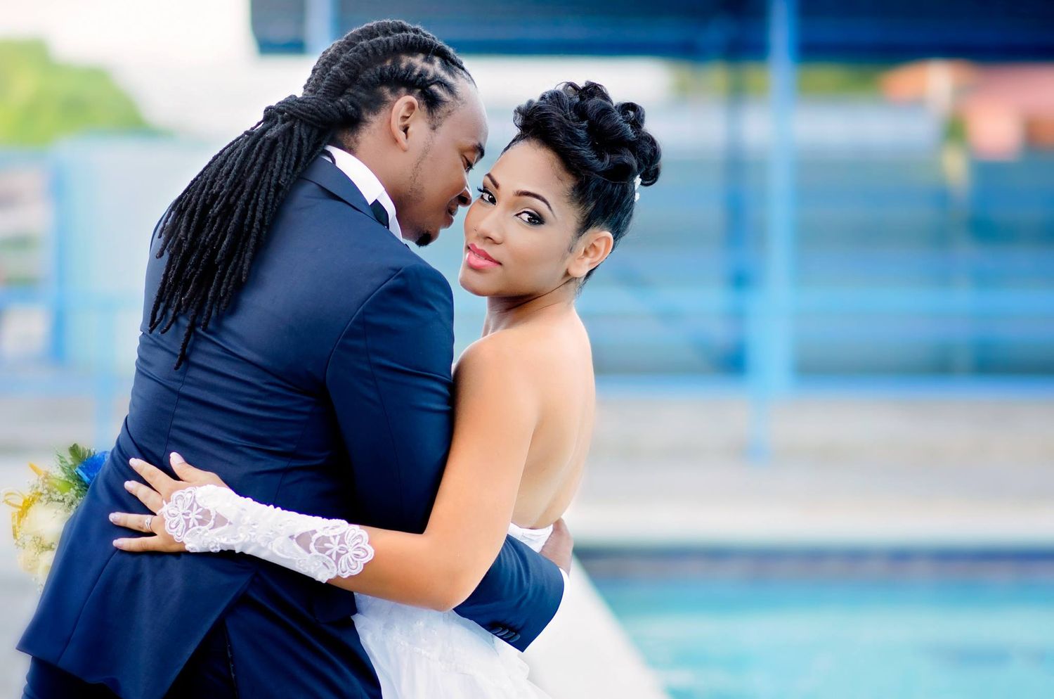 Intimate wedding portrait with couple embracing by pool in formal attire.