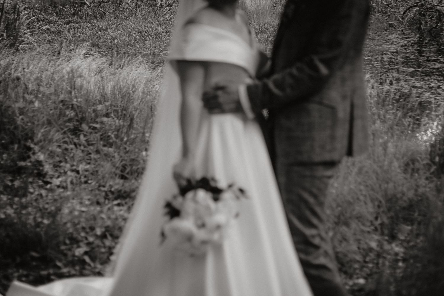A couple walks hand in hand through a garden setting in wedding attire.