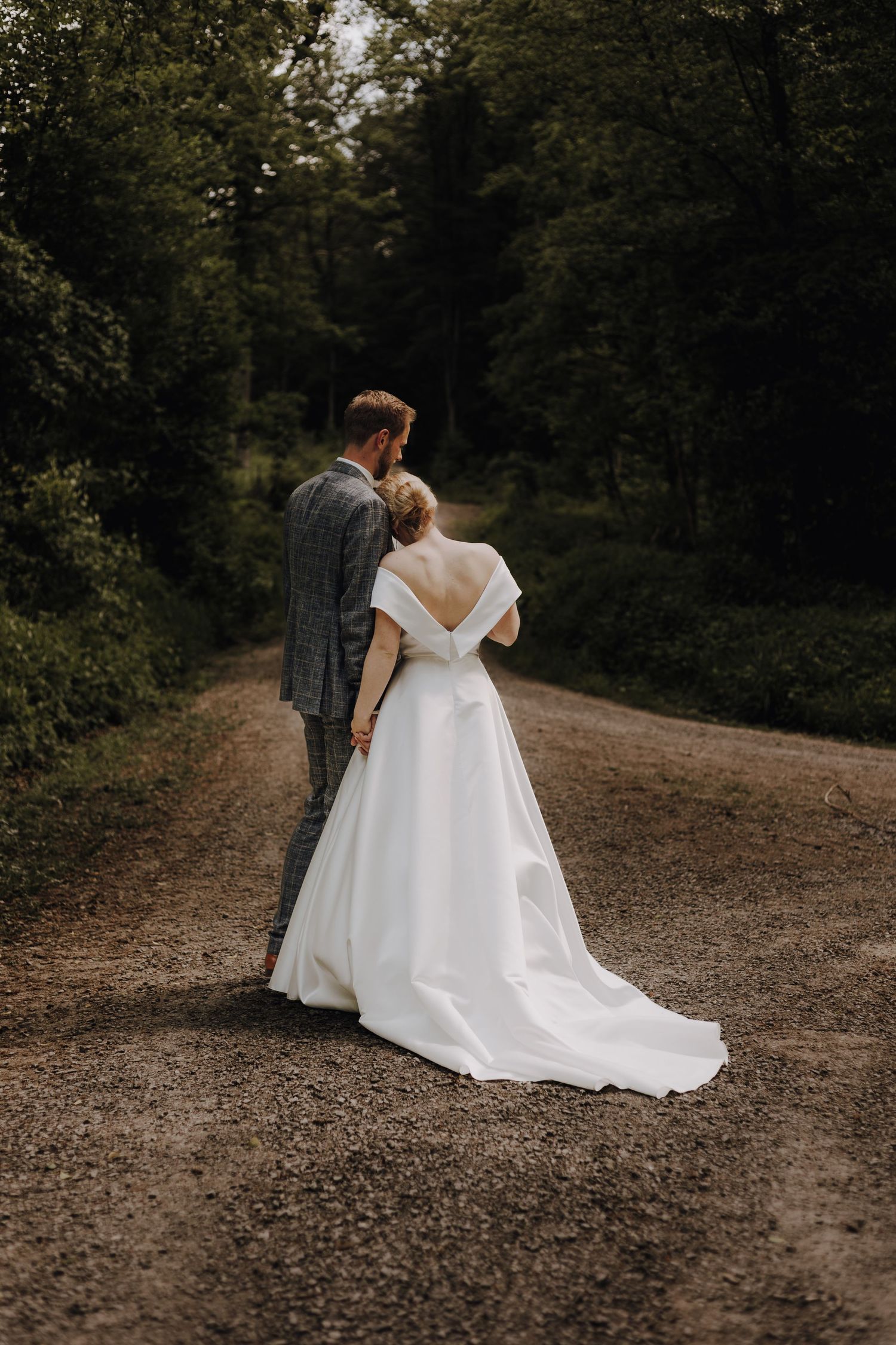 Couple walking along forest path in wedding attire.