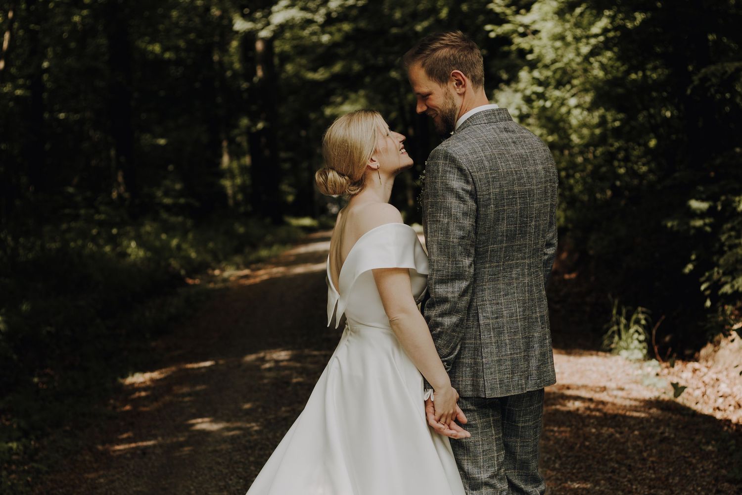 Newlyweds share a romantic moment while walking through a sunlit forest path.