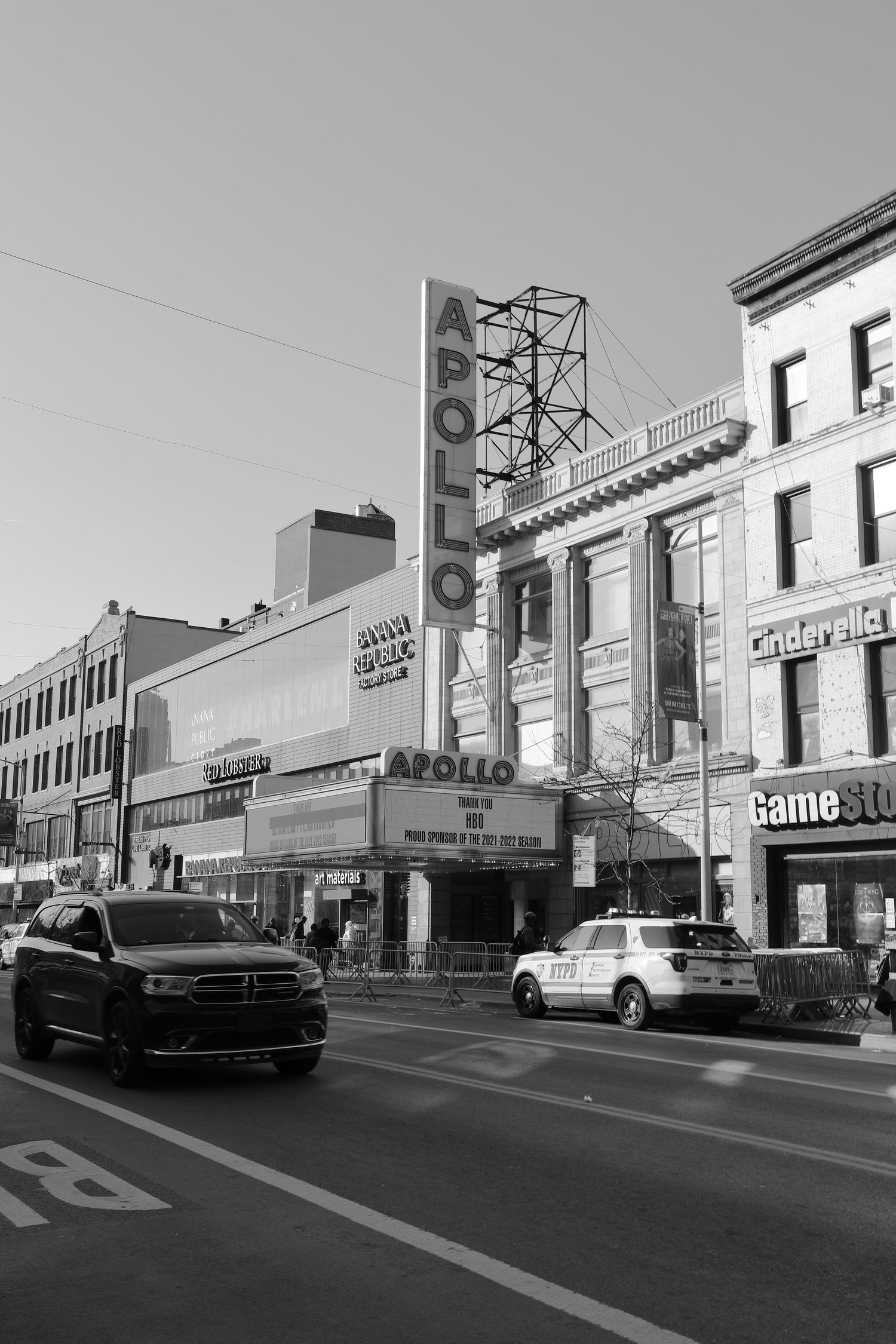 Black and white street view of the historic Apollo Theater in Harlem with cars passing by.