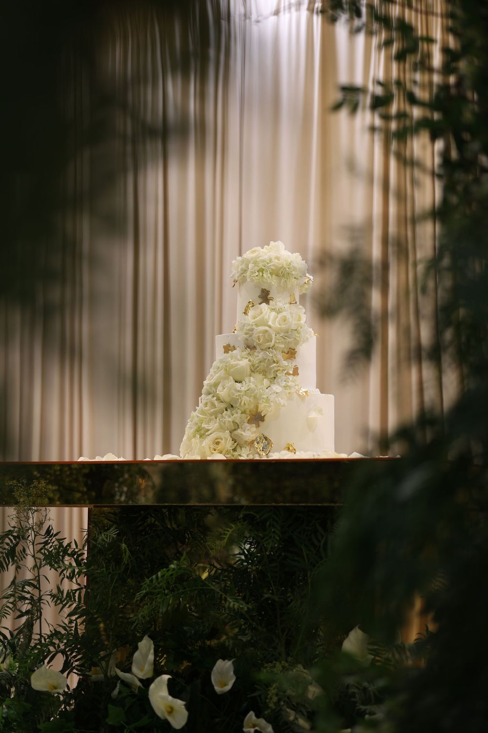 Elegant white floral centerpiece with roses and greenery on tall gold stand adorning formal dining table setting.