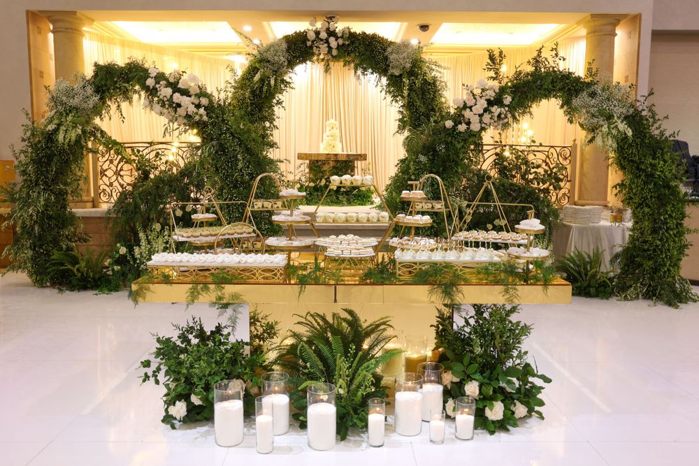 Elegant wedding altar decorated with lush green arches and white floral arrangements in an indoor venue.