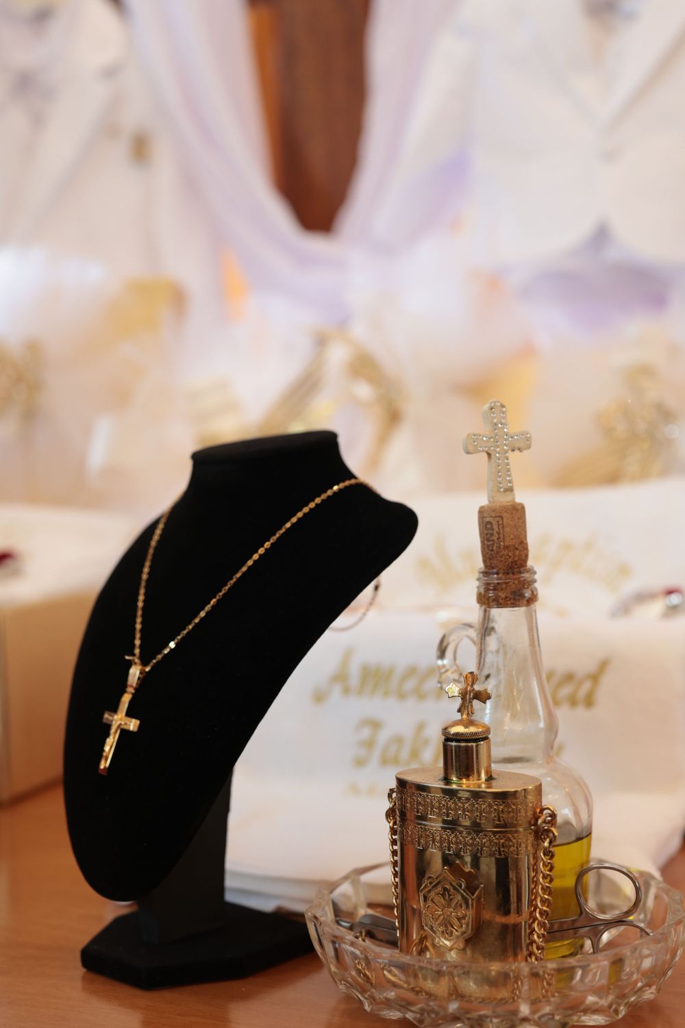 Cross necklace on display stand next to decorative glass bottle in crystal dish.