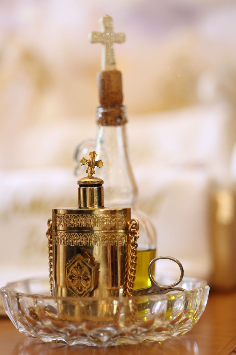 Decorative glass bottle with ornate golden cross stopper displayed in crystal dish.