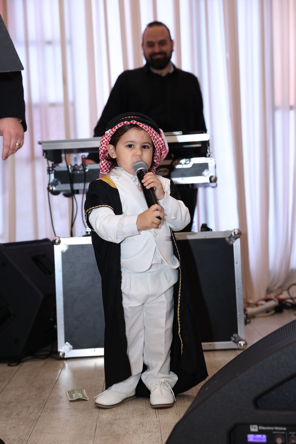 Small figure in traditional white and black attire performs with microphone at formal event.
