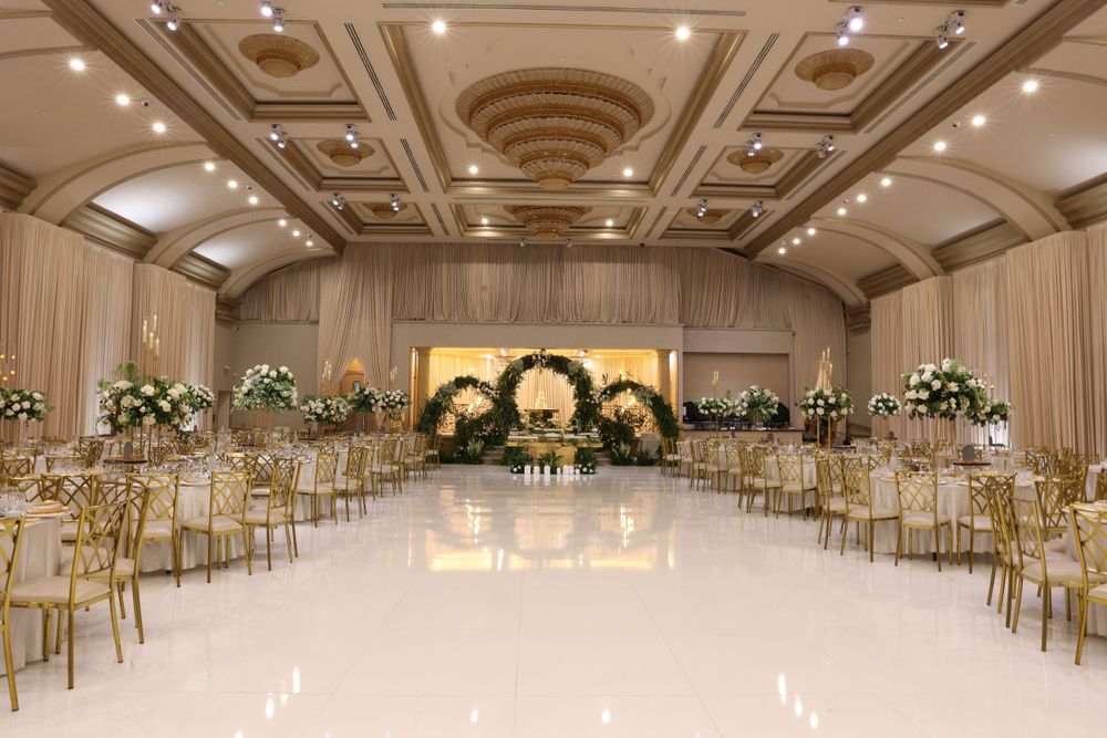 Luxurious ballroom setup with gold chairs and floral arch backdrop for a wedding ceremony.