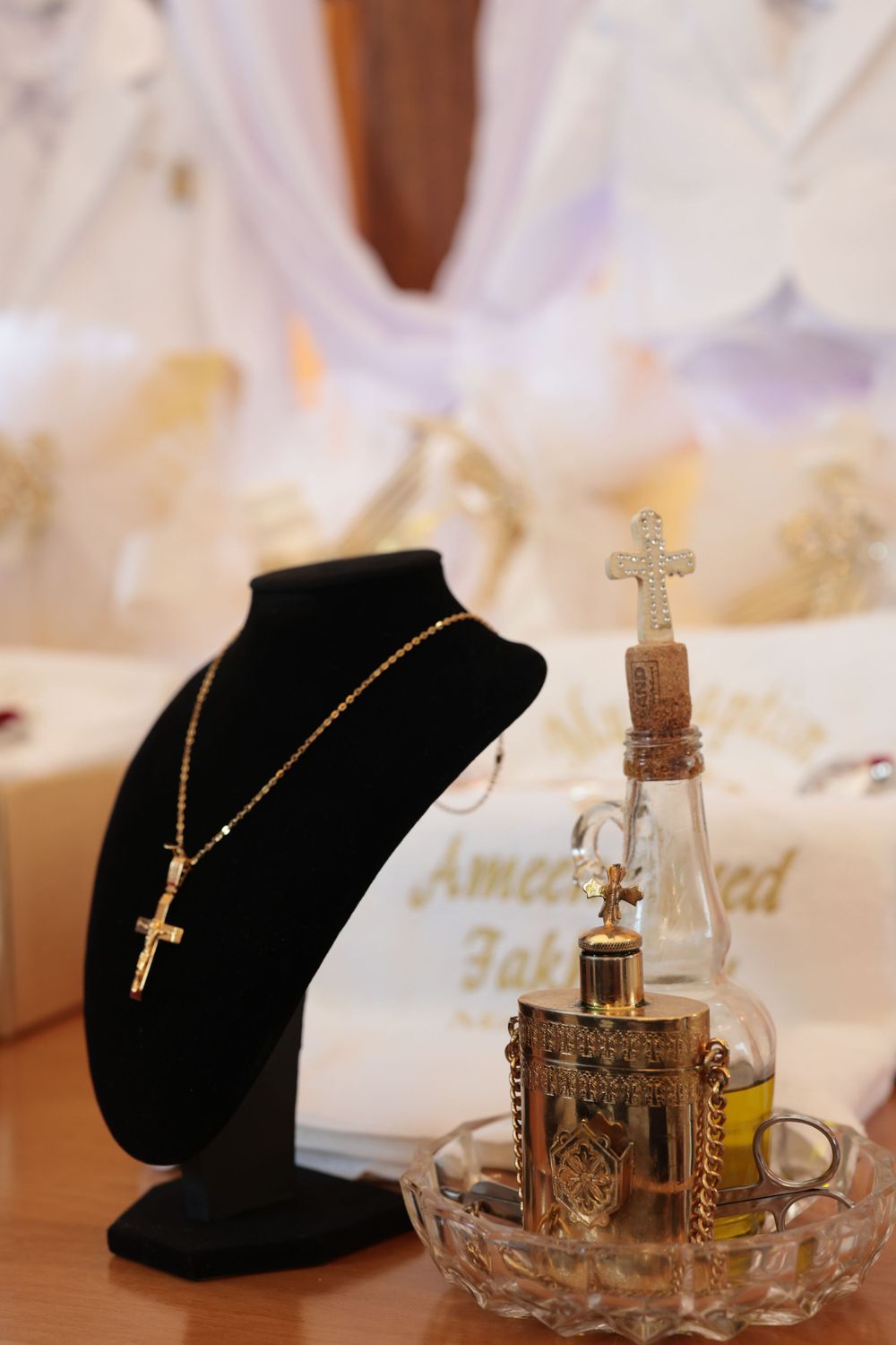 Religious display featuring cross necklace and ornate glass bottle on black velvet stand.