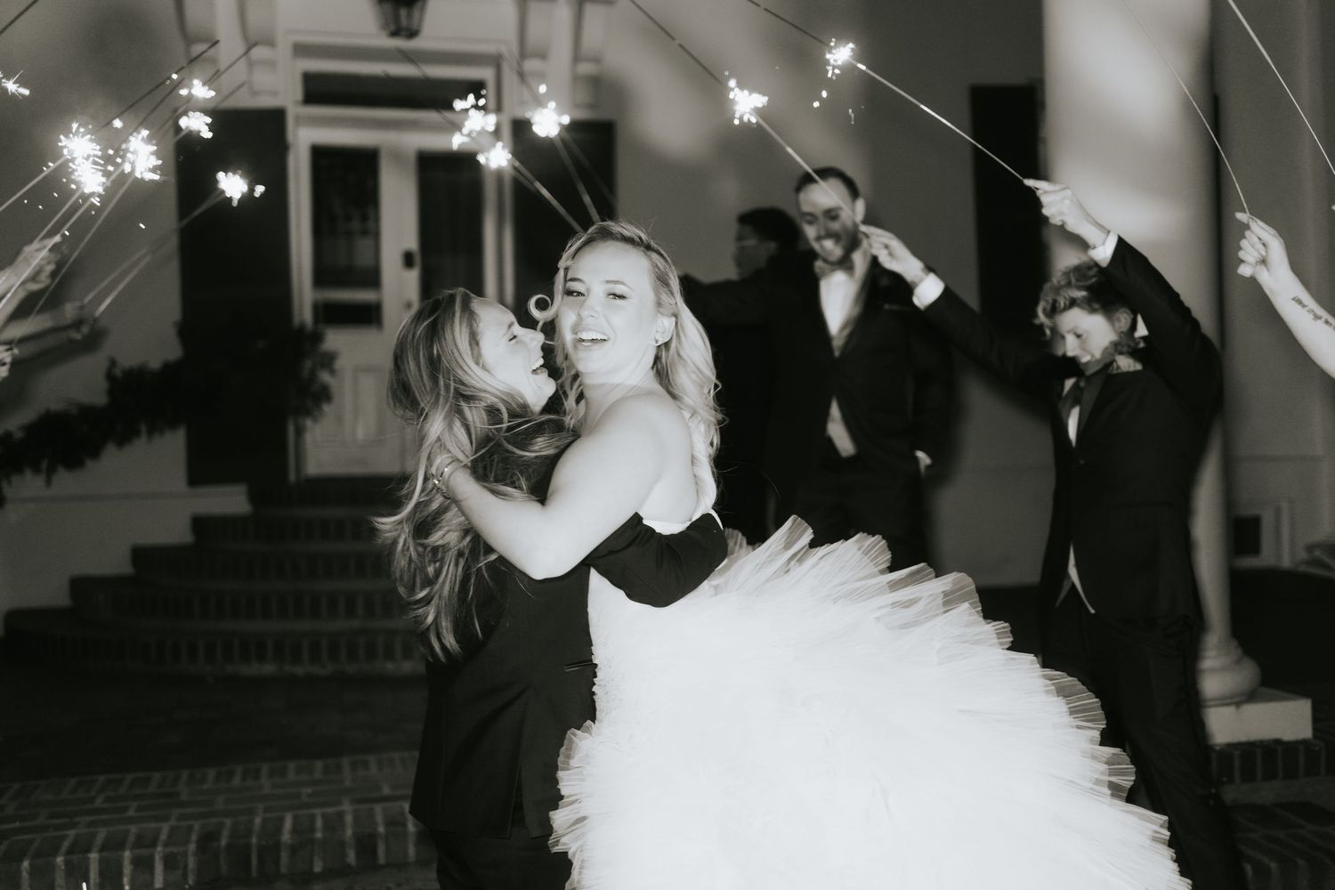 A black and white wedding photo capturing a celebratory moment with sparklers at night.