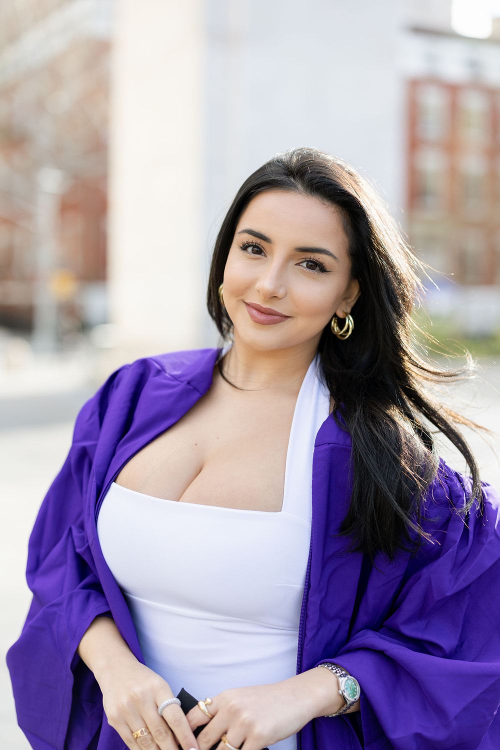 Graduate in white dress and purple graduation gown poses outdoors for portrait.