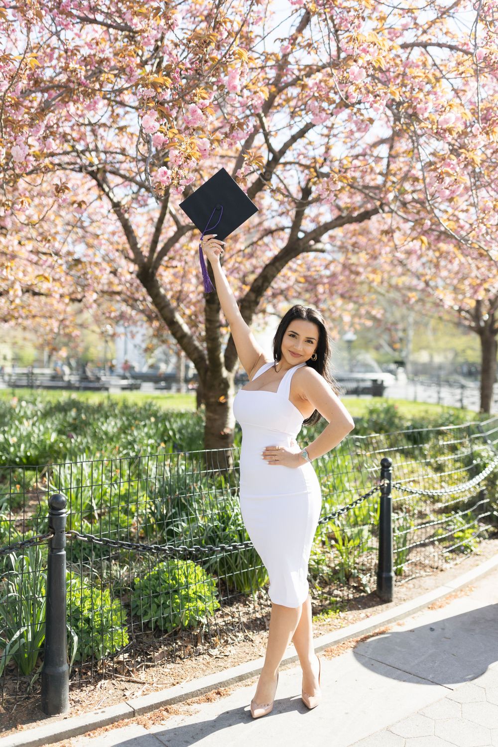 Graduate celebrates by tossing cap near blooming cherry trees in spring.