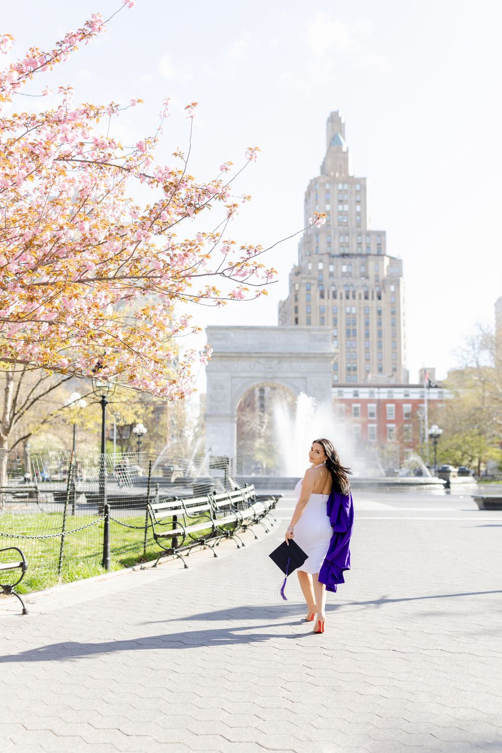 Graduate dances joyfully near Washington Square Arch with cherry blossoms in bloom.