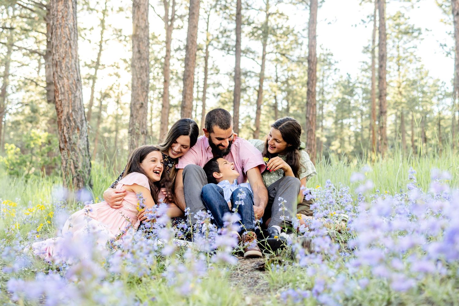 Parents snuggle in the wildflowers with their three young children during their family session in Colorado Springs.