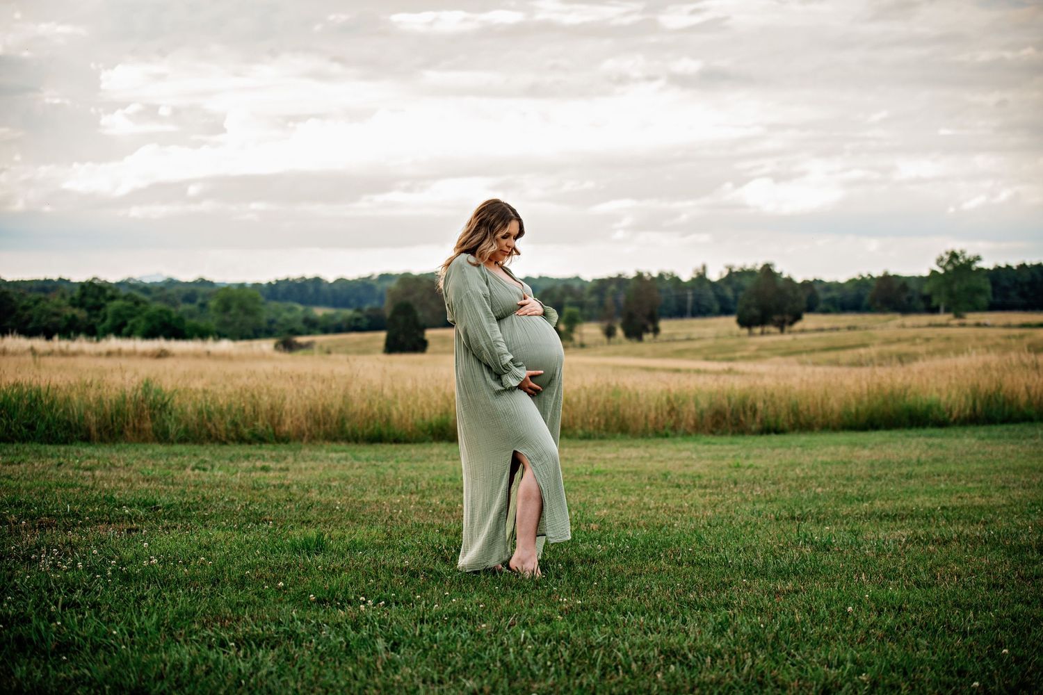 A woman in a light dress stands in profile in a grassy meadow on an overcast day.
