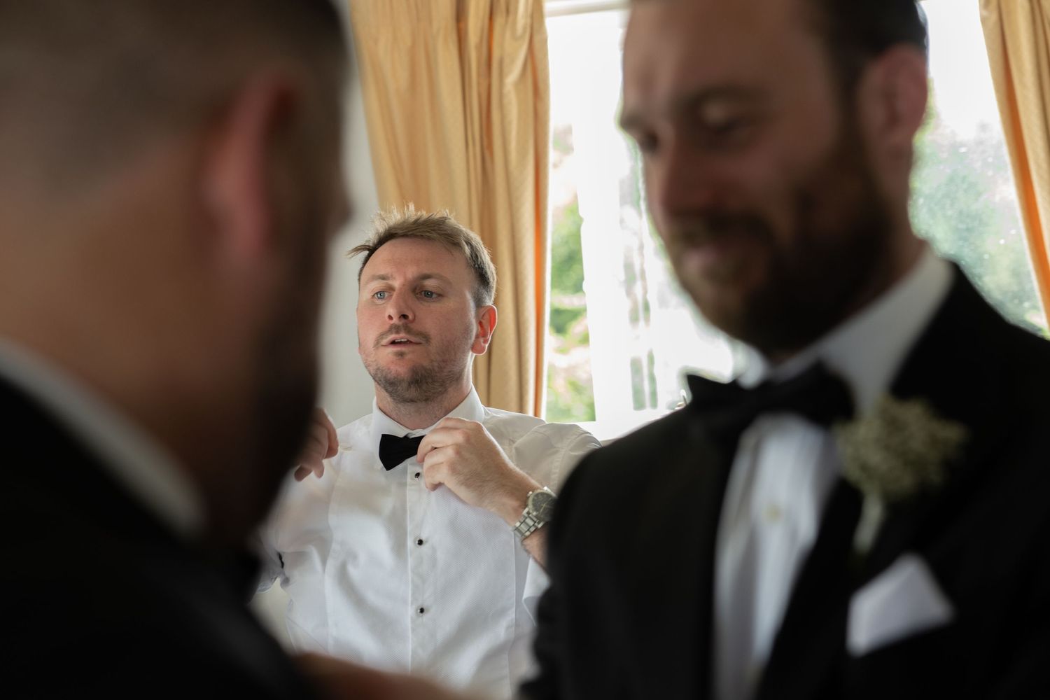 Groomsmen in formal attire adjusting bow ties before the ceremony.