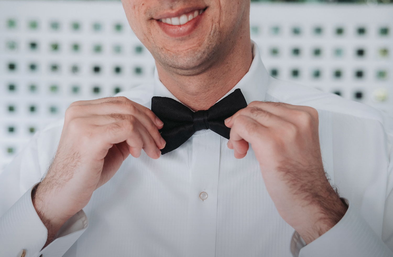 Closeup of hands adjusting a black bow tie on a white dress shirt.