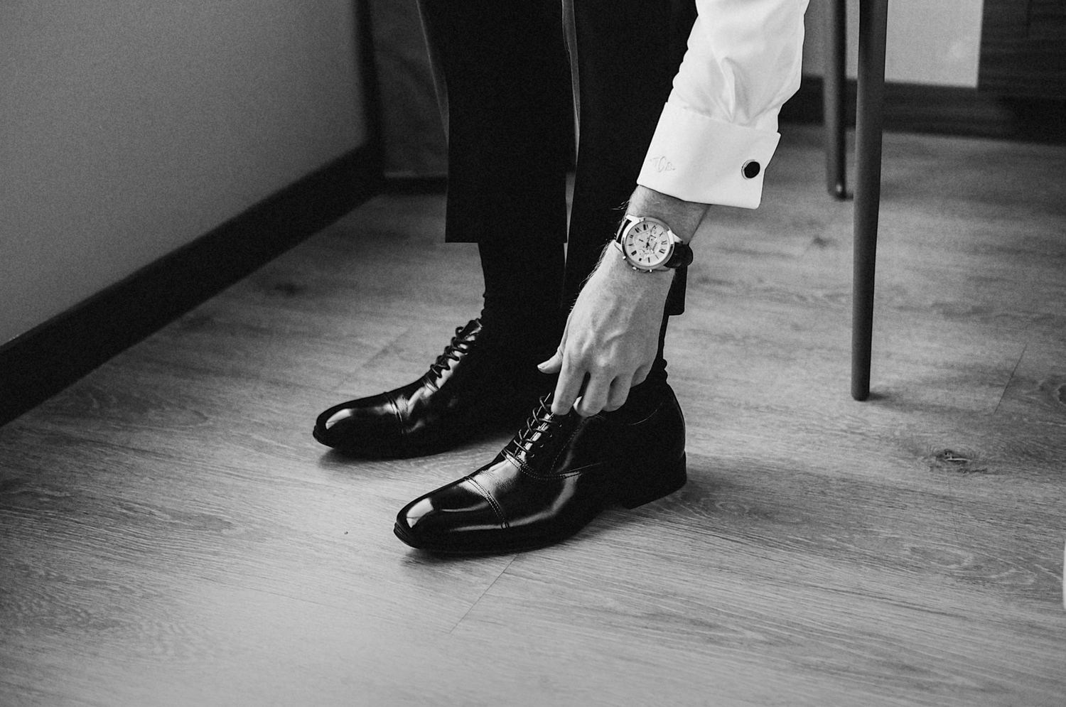 Black and white photo of formal dress shoes being put on wooden floor.