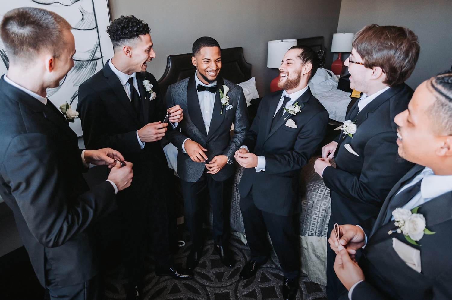 Group of groomsmen in suits sharing drinks and laughs before the ceremony.