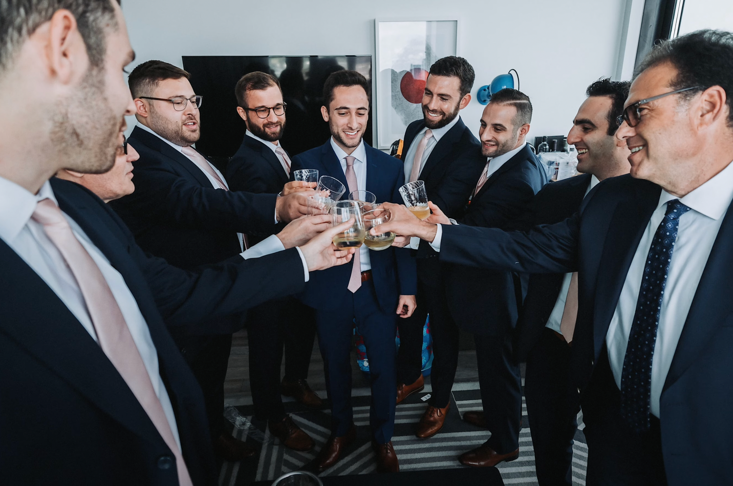 Wedding party in suits toasting with drinks in a circle formation.
