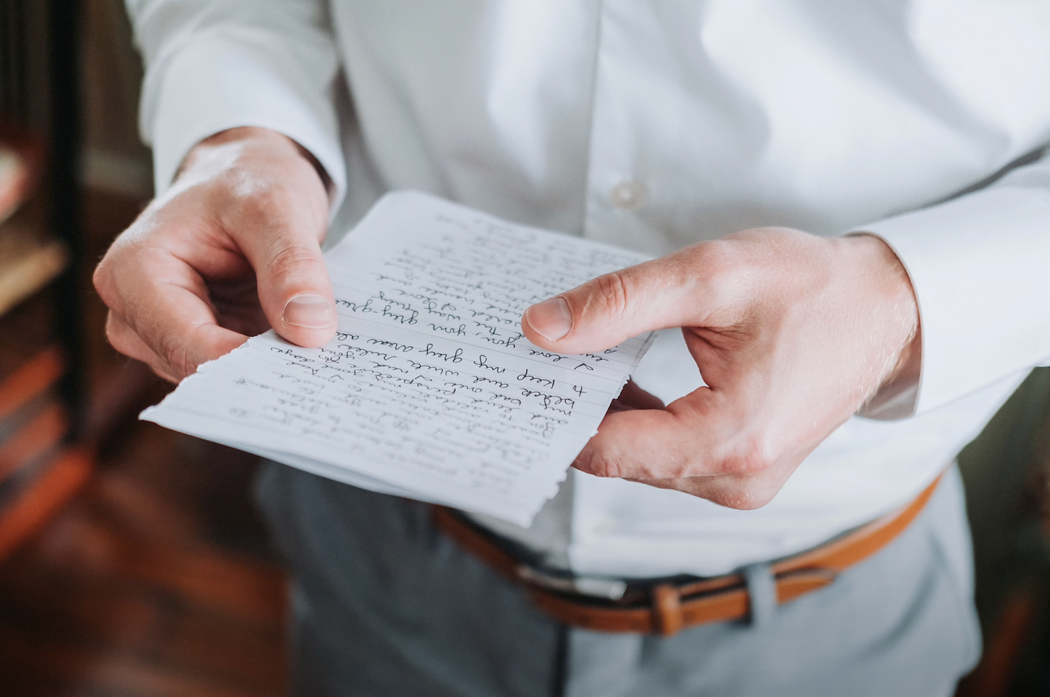 Hands holding a handwritten note in cursive on white paper against a dark background.