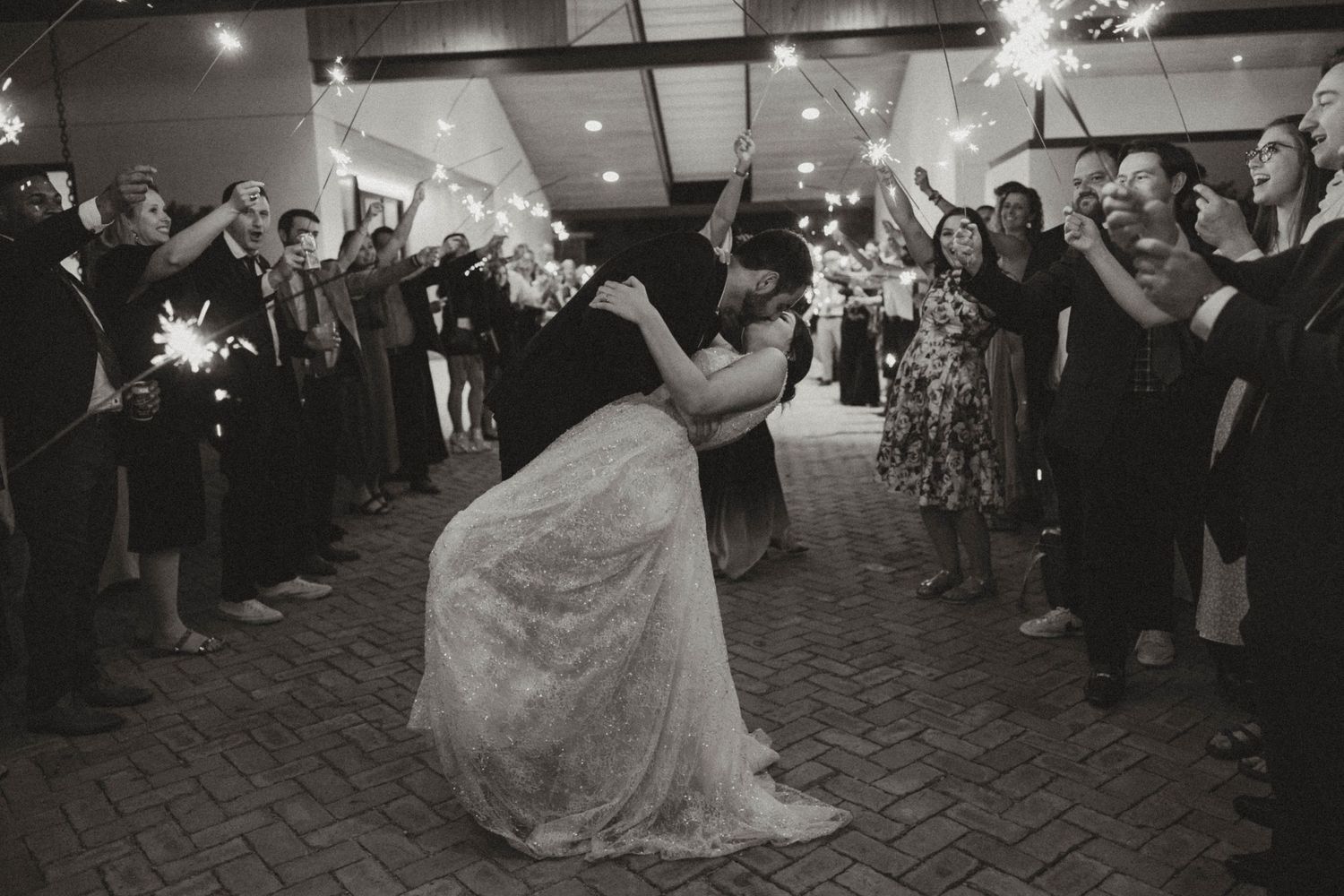 Wedding sparkler exit with guests forming tunnel as couple dips in celebration.