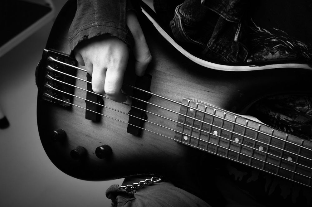 Close-up black and white shot of hands playing bass guitar strings.