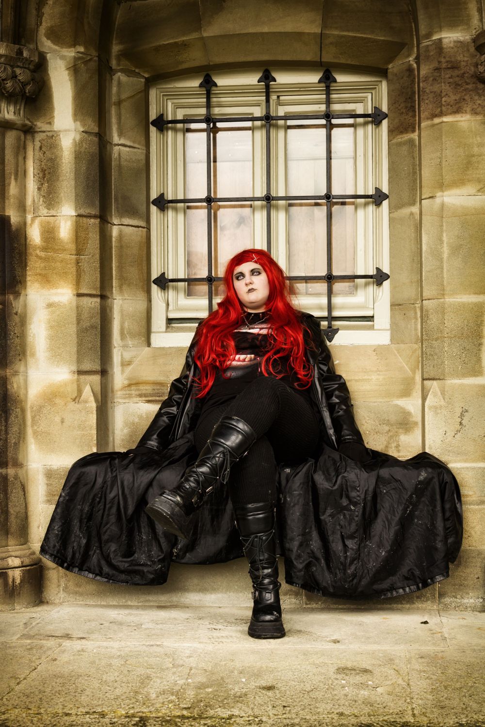 A dramatic portrait featuring flowing black gothic dress and bright red hair in a stone archway.