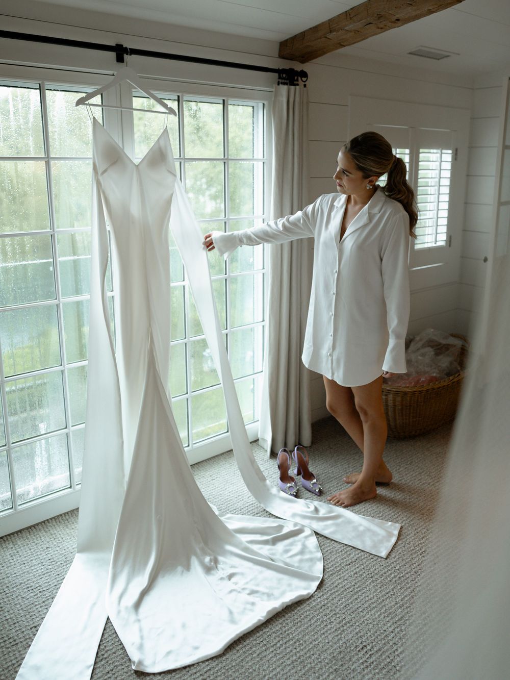 An elegant white wedding gown with a flowing train displayed against bright windows in a sunlit room.