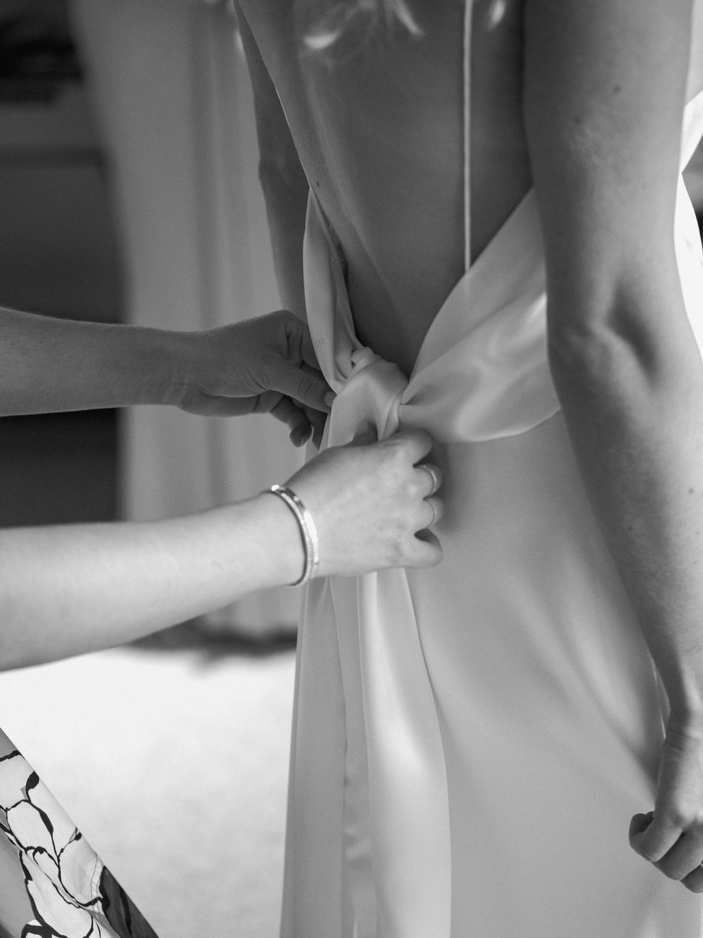 Black and white detail shot of hands adjusting the back of a wedding dress.