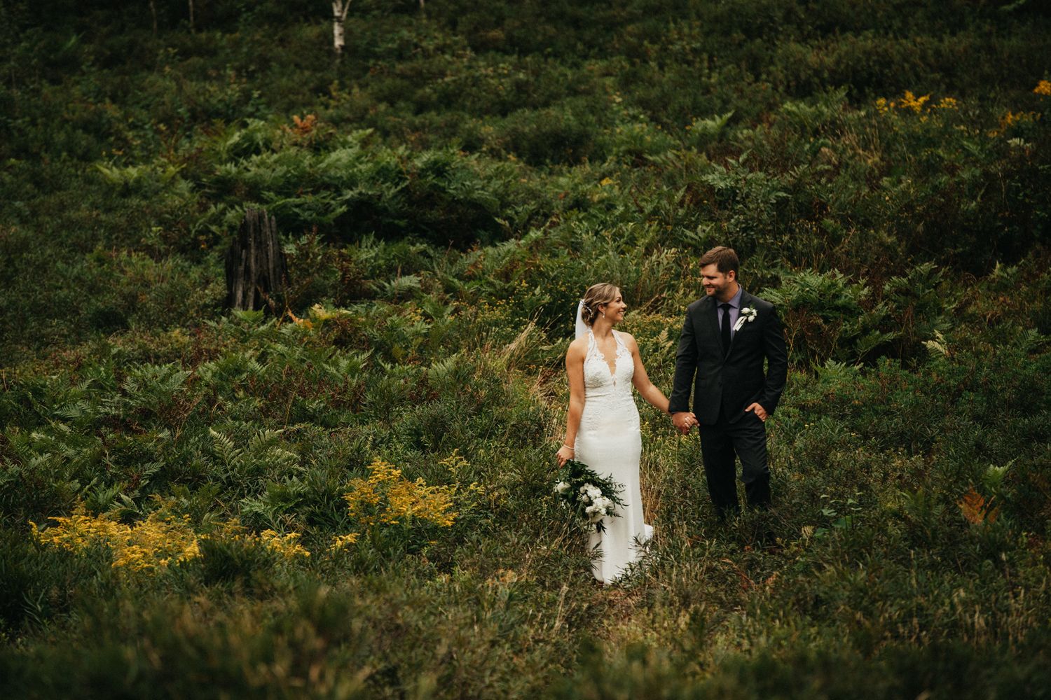 Wedding couple walking through a lush green meadow with wildflowers.