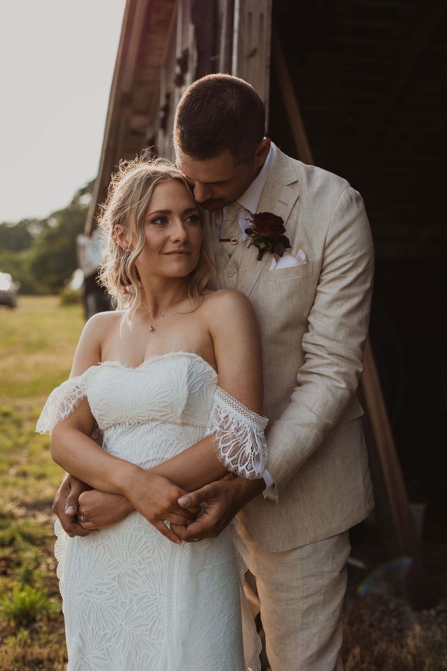 Intimate wedding portrait captured against rustic barn setting in warm evening light.
