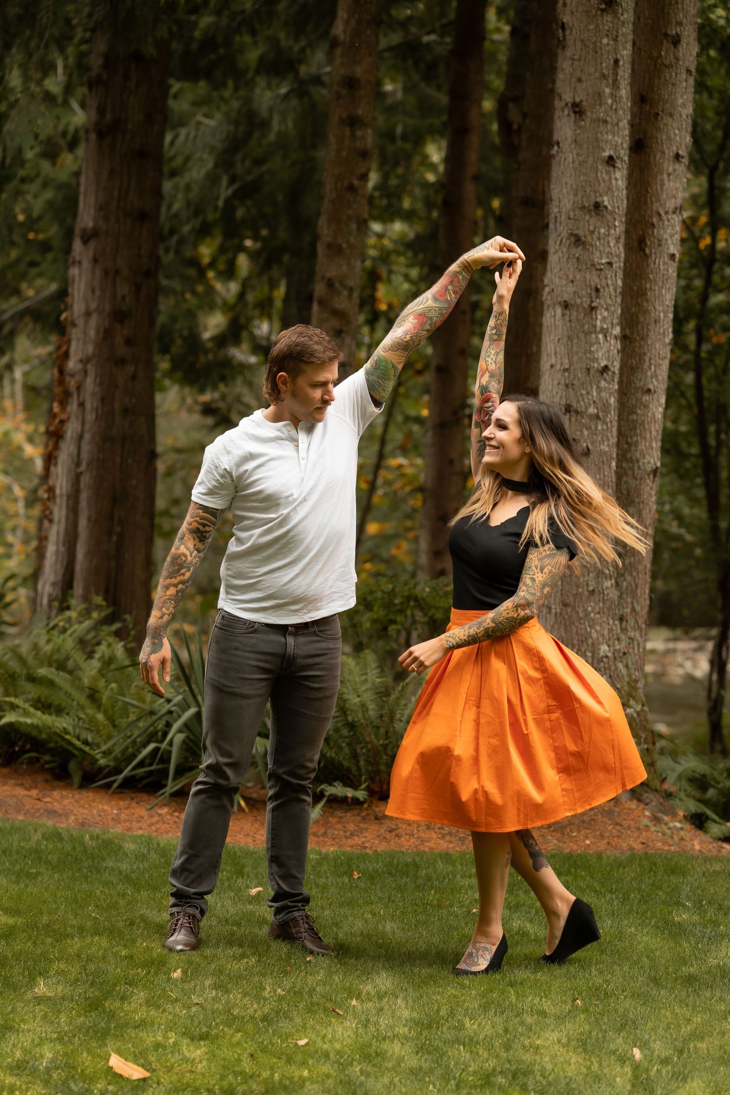 Couple dancing and twirling in a forest setting with the woman wearing a vibrant orange dress.