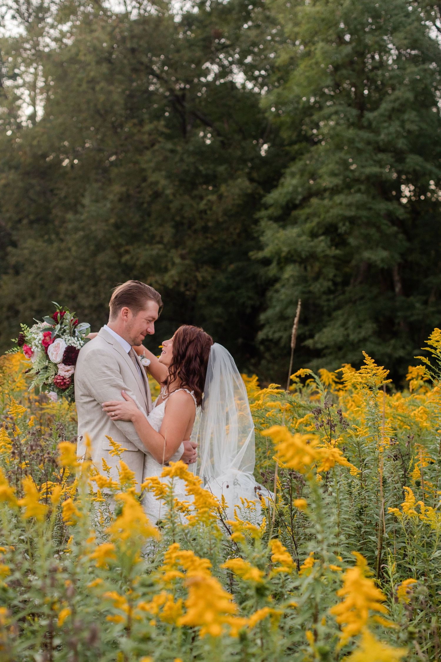 Romantic wedding portrait in a field of vibrant yellow wildflowers with trees in background.