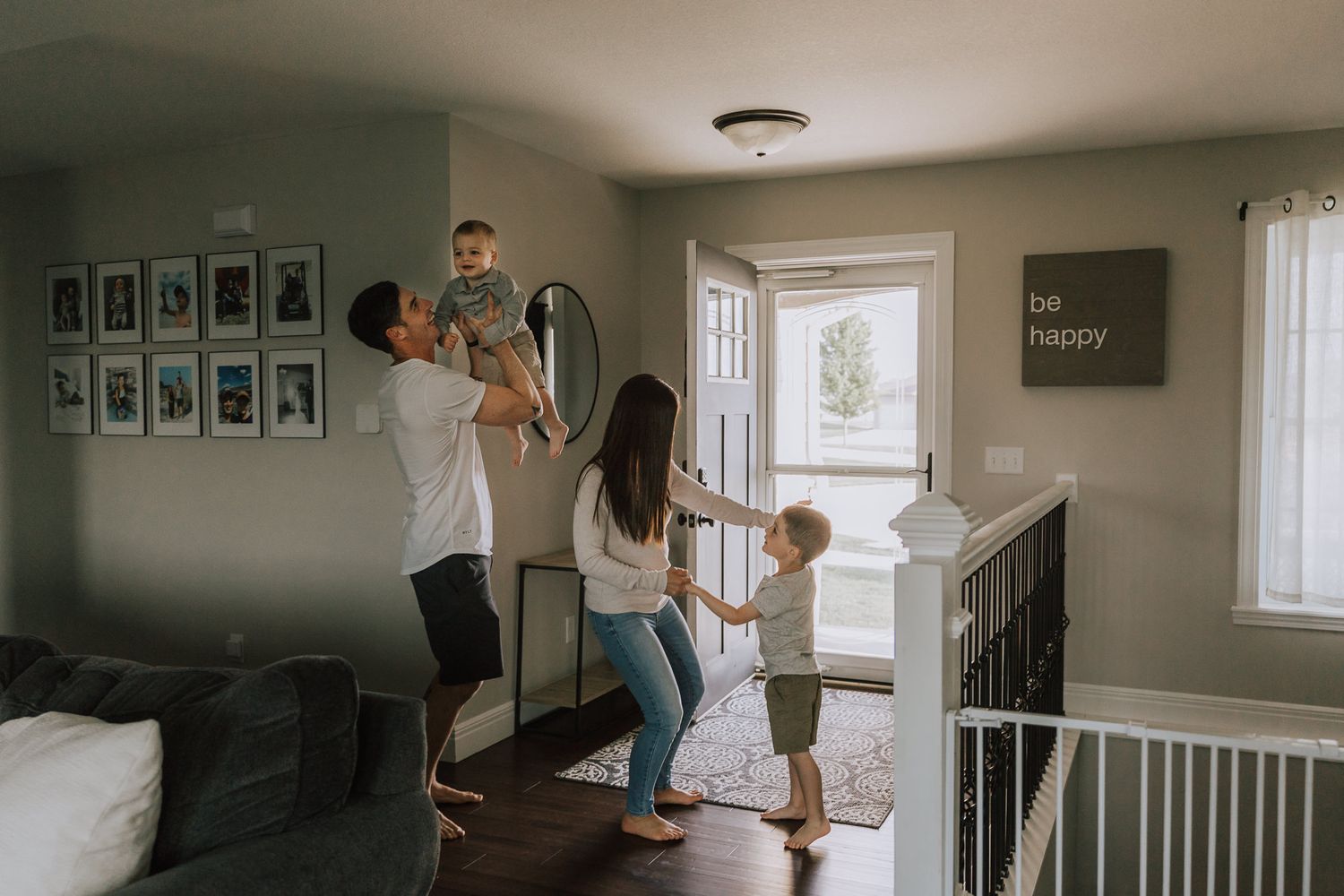 family dancing in their entryway with sunlight shining through their front door with a sign "be happy" in the background