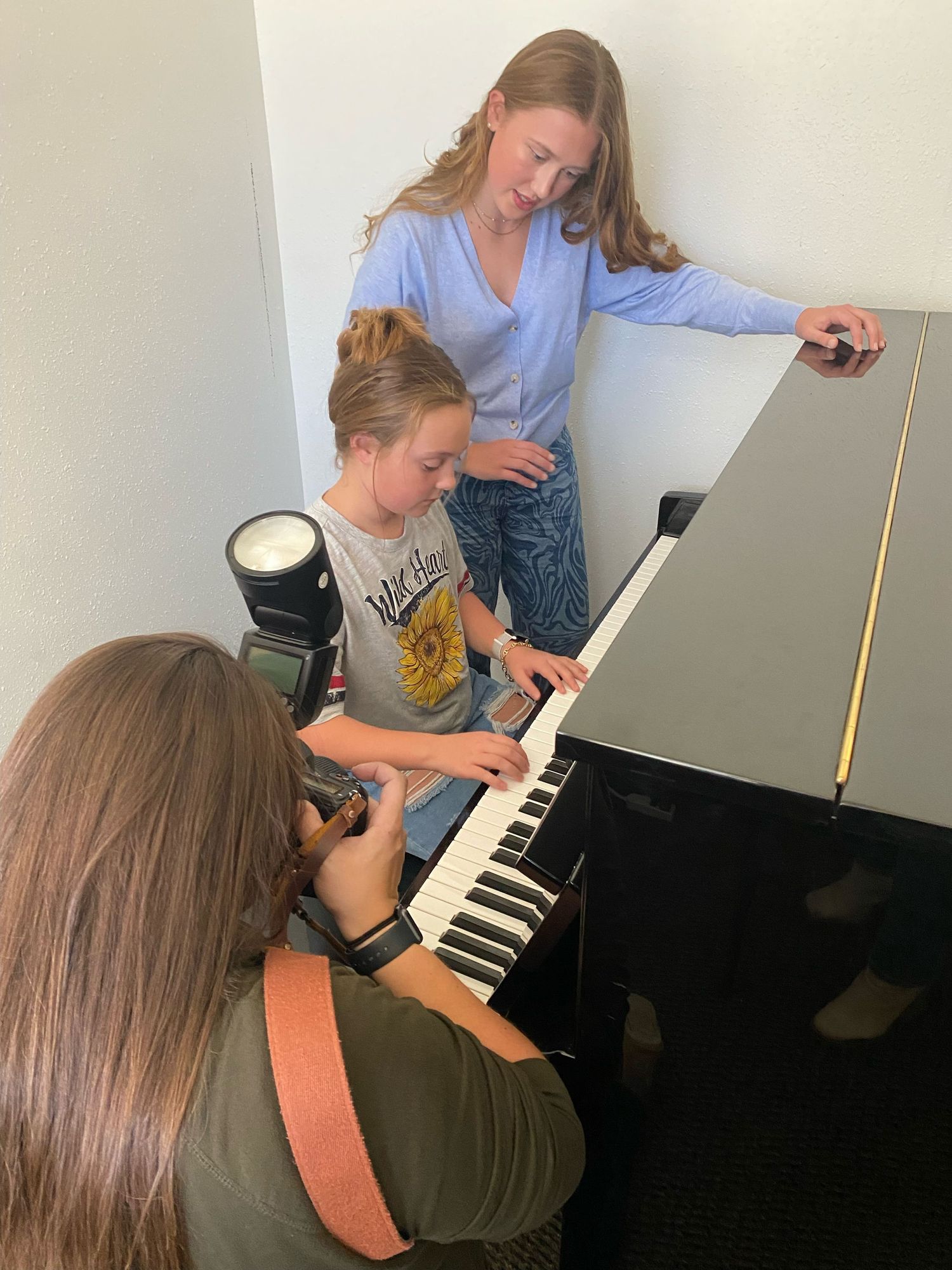 Piano lesson scene with multiple people gathered around a black grand piano.