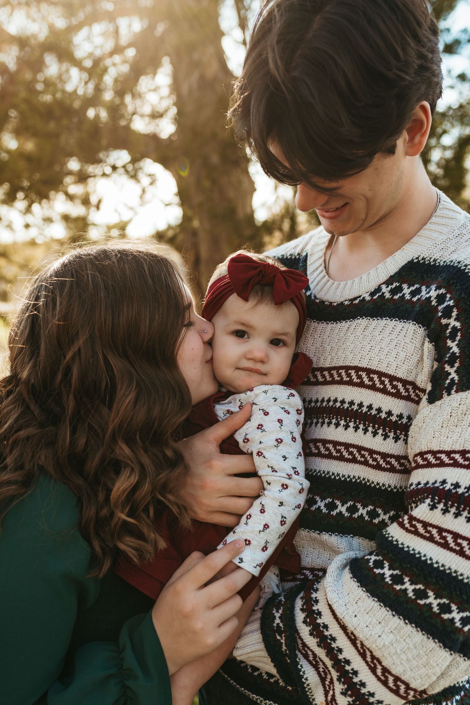 Intimate family moment captured in warm sunlight with winter sweater and baby.